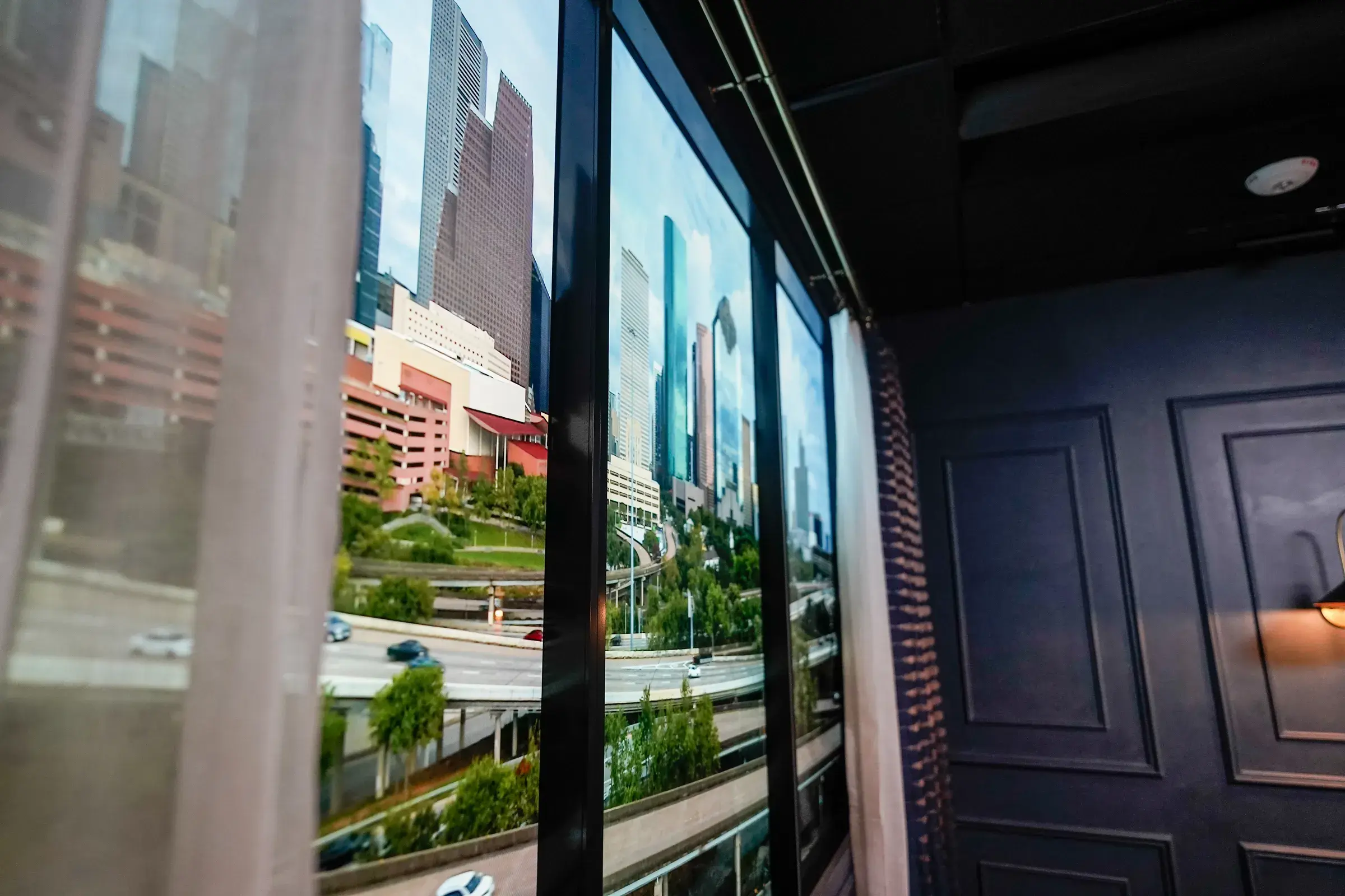 Close view of the finished faux window — the Houston skyline and an elevated highway running across the joined screens behind a sheer curtain