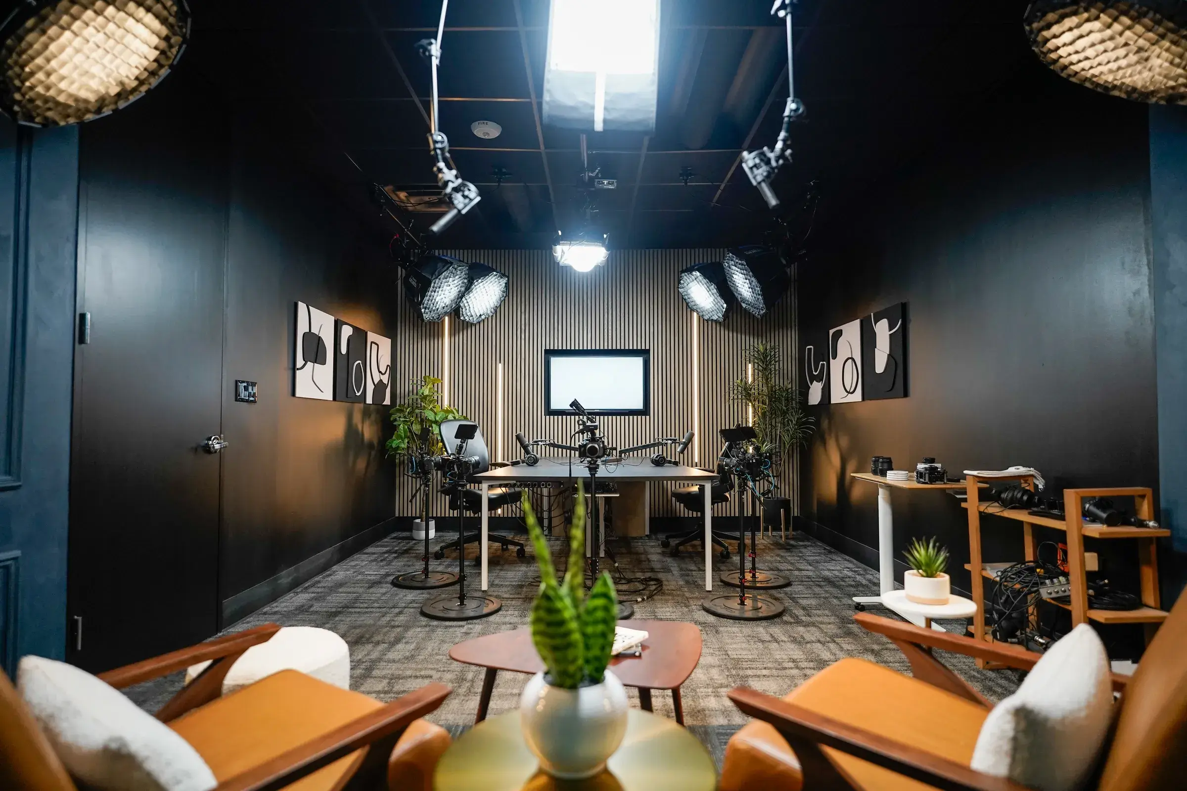 The second studio zone — a podcast desk with microphones on boom arms, a monitor mounted on a slatted acoustic wall, and film lights on stands