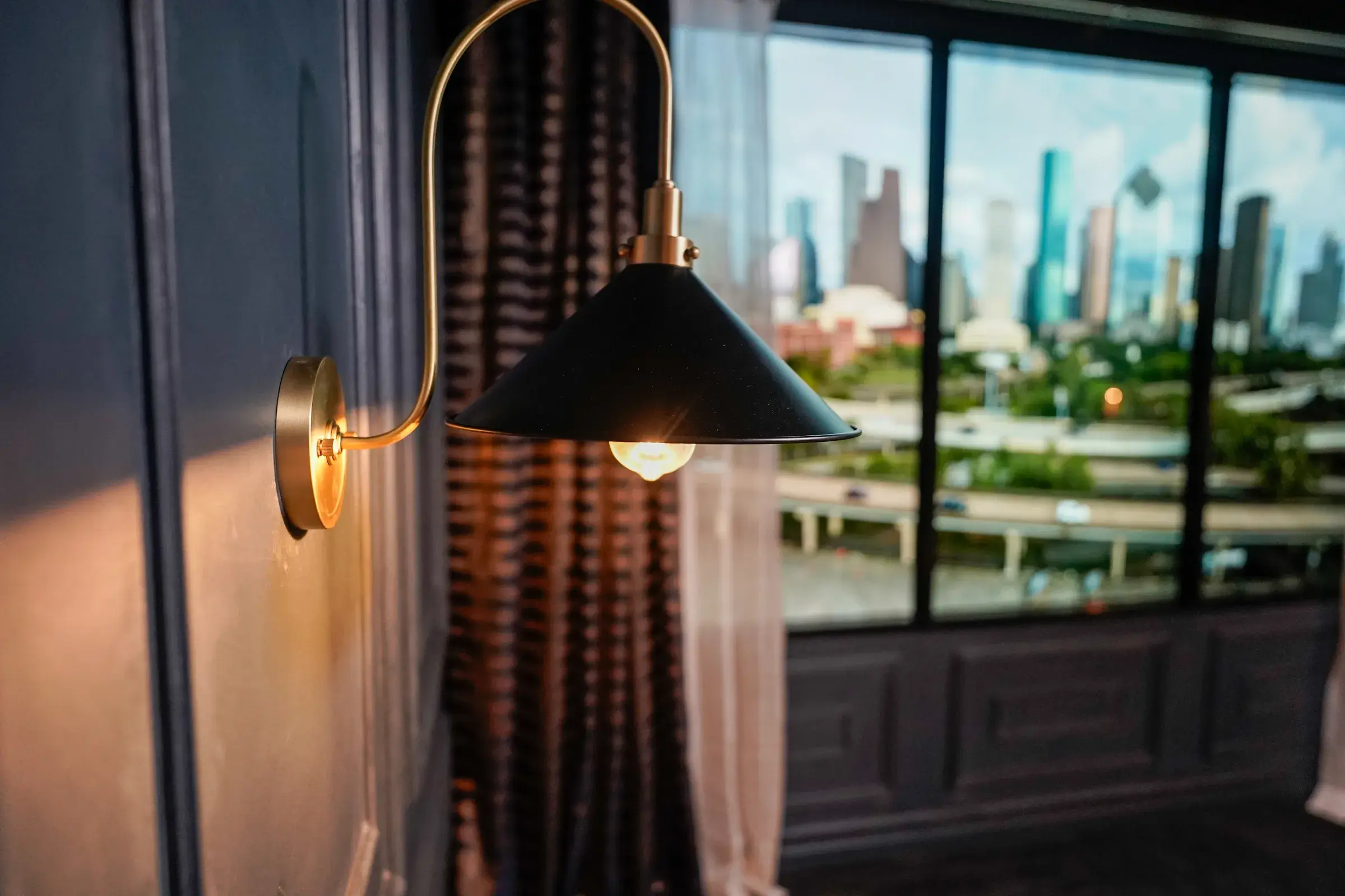 Detail of a brass wall sconce against the paneled wall, with the curtain and window behind it
