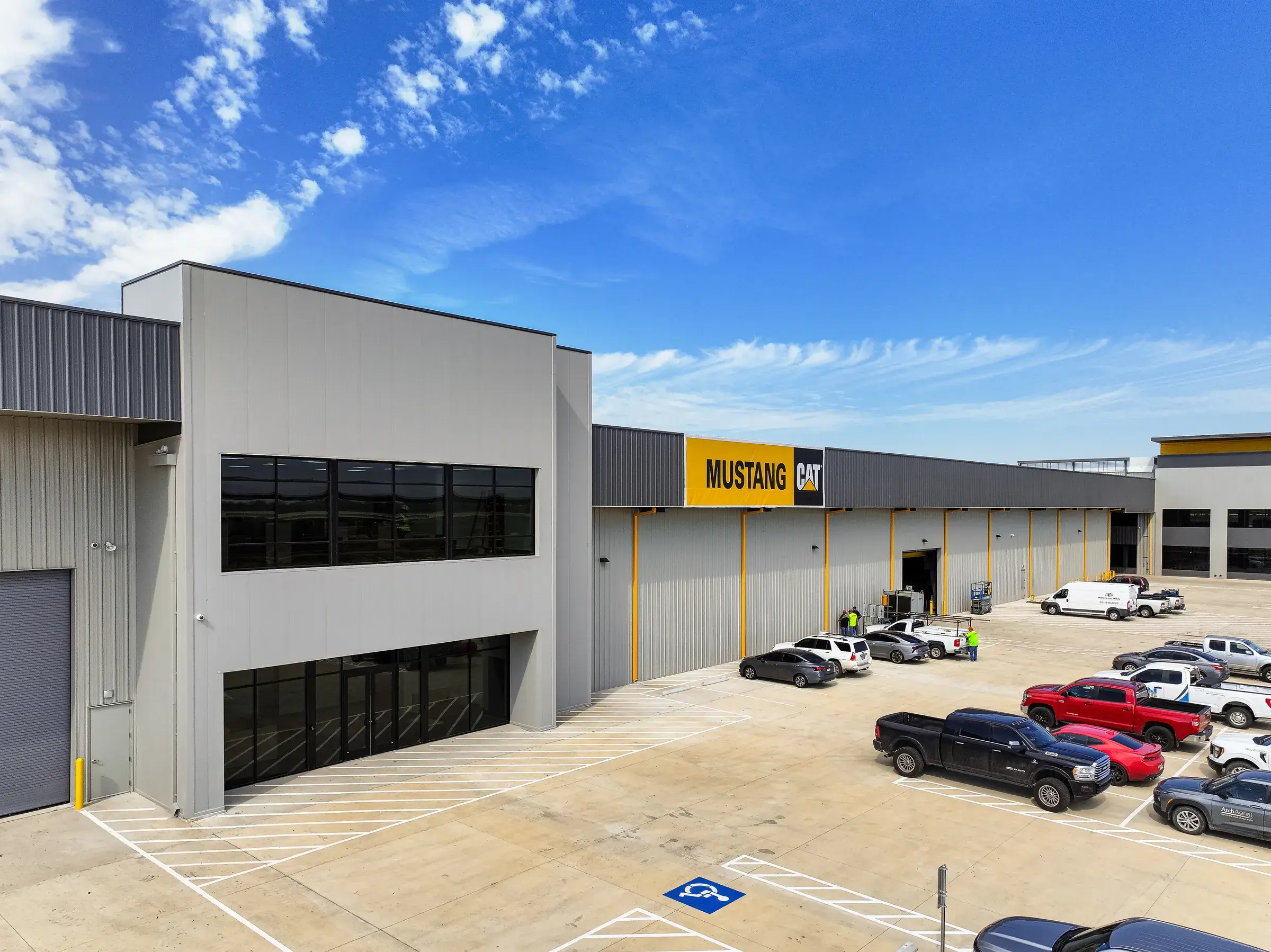 The branded front of the parts and service building, the yellow MUSTANG CAT sign above the bays