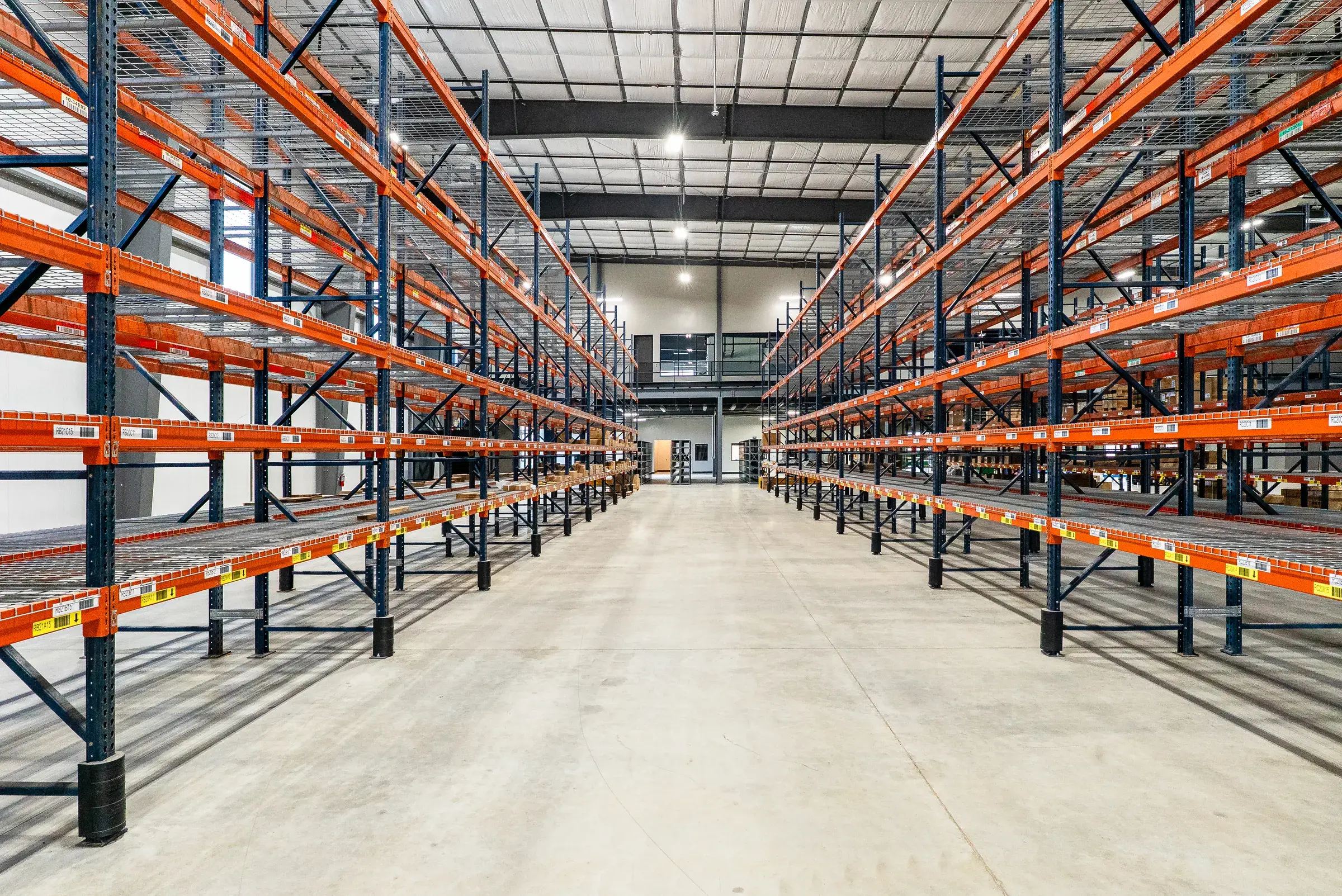 A parts warehouse aisle with orange pallet racking running the full depth of the building