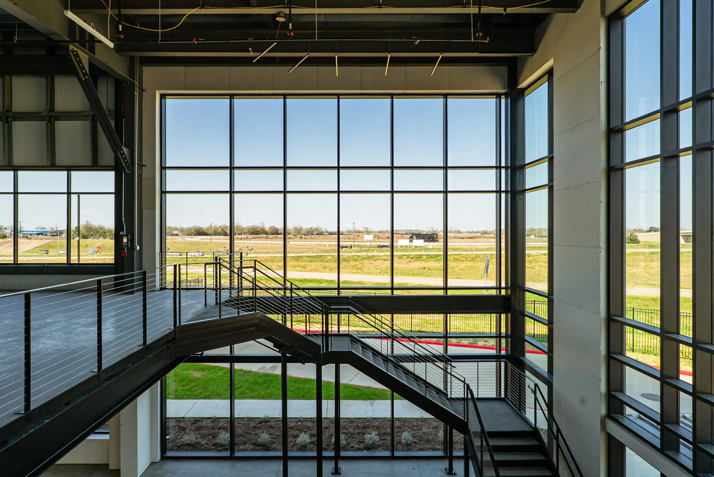 The stair landing inside the two-story glazing, fields visible beyond