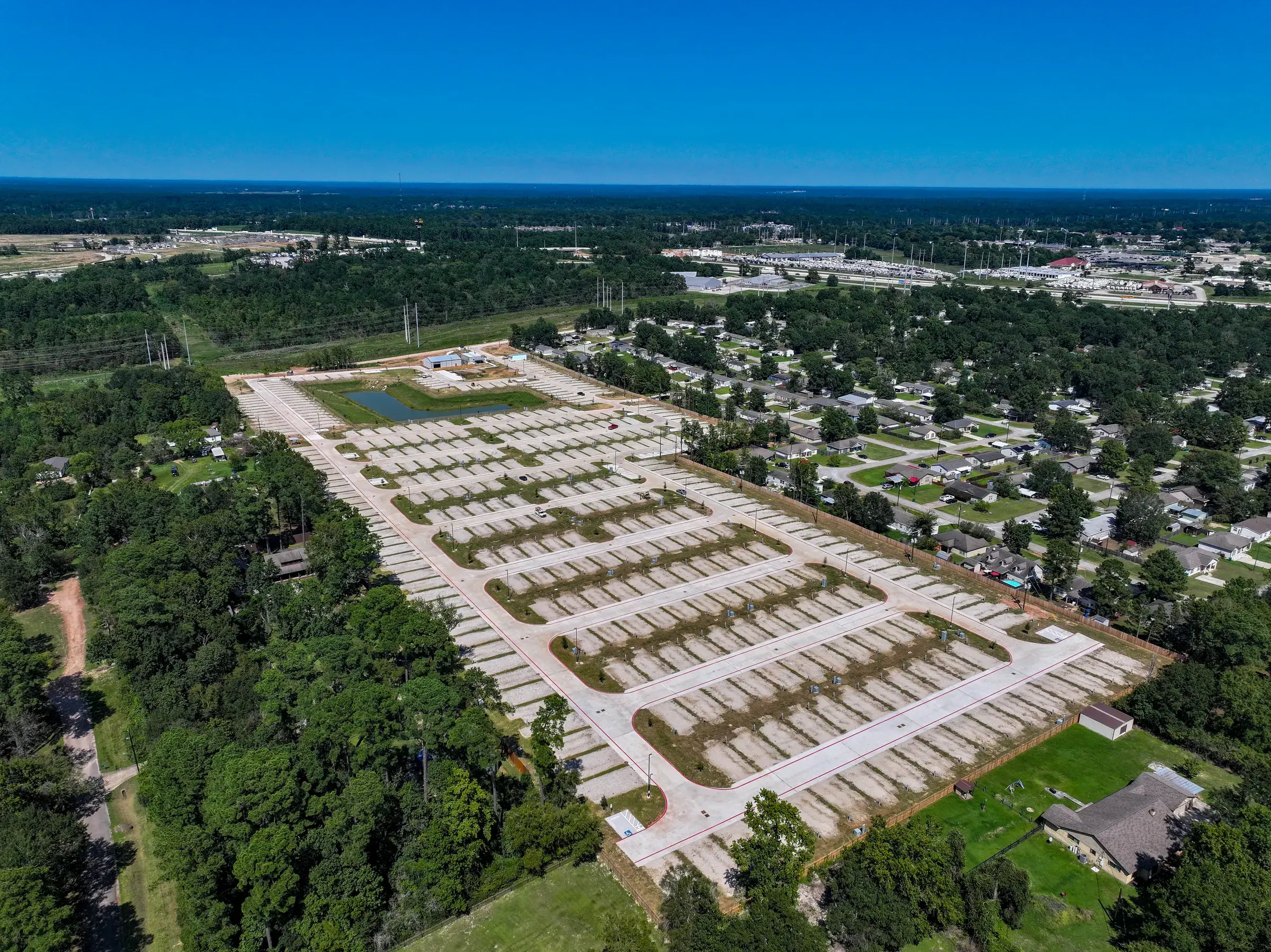 The full development seen from the south — paved streets and pad rows laid out between the tree line and the town beyond